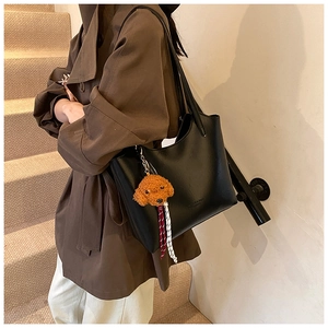 Detail of black leather tote bag with brown dog plush charm on a casual stairway