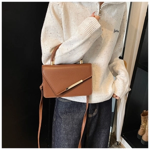 Detail of brown litchi pattern leather handbag with diagonal gold metal bar on flap
