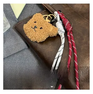 Close-up of brown plush bear charm with woven ropes on a textured tote bag