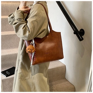 Brown medium tote bag with plush dog charm and scarf shown on model shoulder