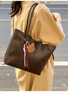 Detailed view of deep brown tote bag with bear charm and texture on a beige trench coat