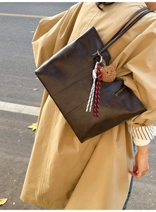 Detail of dark brown leather tote bag featuring a cute plush bear pendant and woven charm