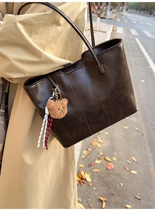 Detail of dark brown tote bag with vintage texture and plush bear charm on shoulder