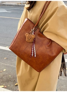 Brown PU leather tote bag with plush bear charm worn with a stylish autumn trench coat