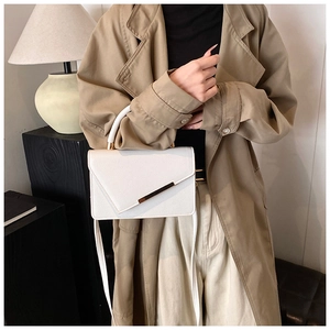 Detailed close-up of white leather handbag featuring asymmetric fold and gold metal trim