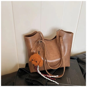 Close-up of brown faux leather tote bag featuring a cute plush puppy charm accessory