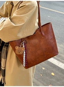 Close-up of brown leather tote bag with plush bear charm and woven rope decoration