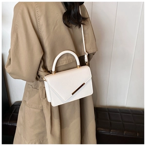 Detail of white litchi pattern crossbody bag with gold hardware on a trench coat model