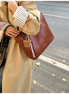 Close-up of caramel tote bag with plush bear charm on beige trench coat in autumn