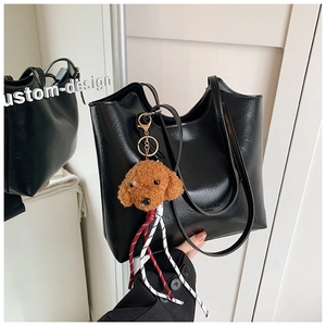 Detail of black pebbled leather tote bag featuring a cute brown poodle plush charm