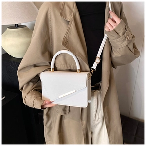 Chic off-white crossbody bag with lychee texture and gold metal bar held by a model