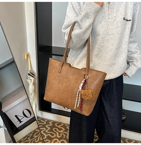 Detailed close-up of brown textured leather tote bag with cute bear charm and strap
