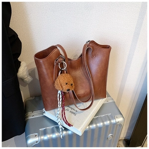 Detail of dark brown tote bag with leather texture and cute teddy bear charm on luggage
