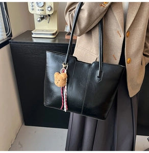 Detail of black faux leather tote bag with vertical stitching and brown bear charm