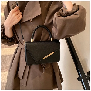 Detail of black lychee leather crossbody bag with asymmetrical gold bar flap design