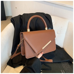 Braune Handtasche mit Litschi-Textur und goldenem Metallstab auf Sessel mit Sakko