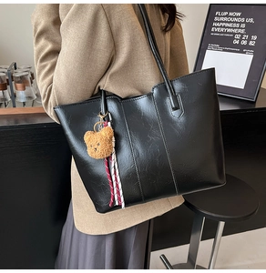 Detail of black textured leather tote bag featuring a cute plush bear charm for daily commute