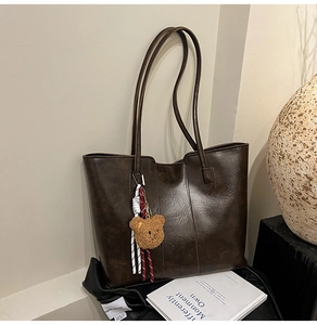 Detail of dark brown faux leather tote bag with cute plush bear charm decoration