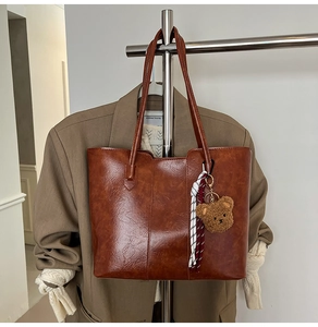 Detail of brown faux leather tote bag with cute bear charm and woven rope accessory