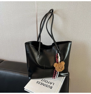 Detail of black glossy faux leather tote bag featuring a cute brown plush bear charm