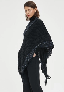 Detalle del tejido de punto y flecos de un poncho negro con rayas para mujer