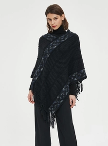 Detalle del poncho de punto negro con patrones geométricos y flecos largos