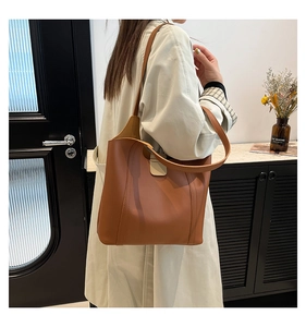 Brown leather tote bag side view on model highlighting the spacious bucket design