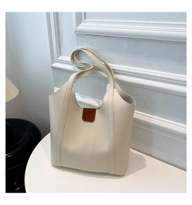 Detail of minimalist cream tote bag with brown leather patch on a white table