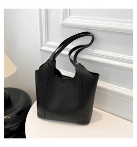 Close-up of minimalist black tote bag with wide straps on white table surface