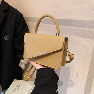 Schicke beige Umhängetasche mit goldenen Details, getragen zu einem schwarzen Anzug