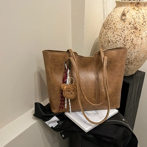 Brown faux leather tote bag with teddy bear pendant on neutral vintage background