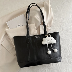 Detail of black textured tote bag with detachable plush cloud charm and long straps