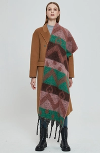Full view of thick geometric jacquard winter scarf with long black tassels and camel coat