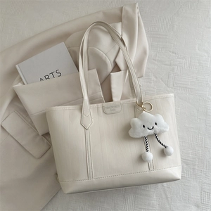 Detail of cream tote bag with wave texture, logo, and cloud plush charm on a blazer