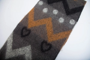 Detail of thick knit scarf showing grey base with orange zigzag and heart patterns