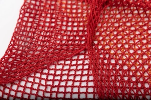 Detail of red mesh knit shawl with gold metallic threads and elegant tassel fringe