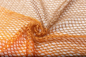 Macro shot of gradient orange mesh knit fabric with metallic luster and tassel detail