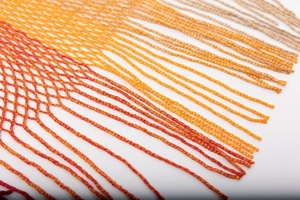 Detailed macro shot of gradient mesh knit shawl featuring vibrant fringe and tassel finish