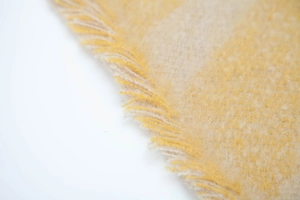 Detail of yellow and beige plaid scarf showing soft fuzzy texture and fringe edges