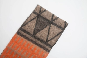 Detail of chunky knit scarf with orange and brown geometric patterns and tassel texture