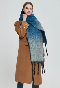 Detail of blue-green gradient scarf with thick tassels on a caramel wool coat