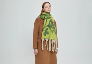 Detailed texture of thick mohair scarf with artistic green floral patterns and tassels