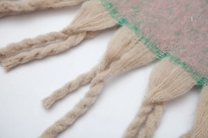 Detail of pink and green gradient knit scarf featuring thick off-white twisted tassels