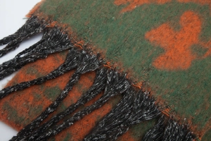 Macro shot of forest green and orange textured scarf with long tassels and fiber detail