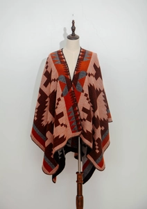 Dettaglio di un poncho in maglia bohémien con motivi geometrici arancioni e marroni