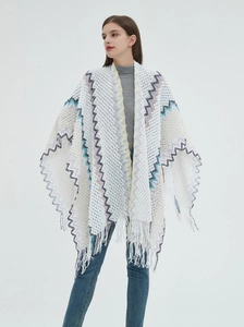 Detail of white knit poncho featuring colorful wave patterns and long tassel hemline