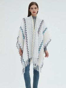 Detailed shot of white knit poncho featuring colorful wavy patterns and long fringe hem