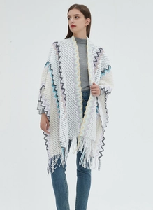 Detailed close-up of white knitted poncho featuring colorful wave patterns and fringe hem