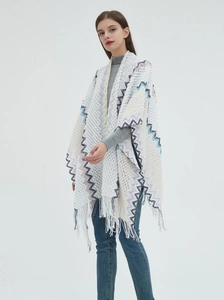 Close-up of white knit poncho with colorful tribal patterns and fringe details on the hem
