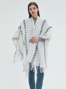 Close-up of bohemian white knitted shawl featuring colorful wave patterns and fringe trim